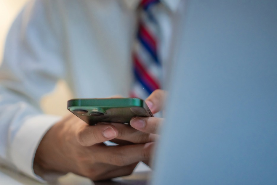 man in a white shirt and red striped tie holding a cell phone at a desk. only his chest and shoulder are visible